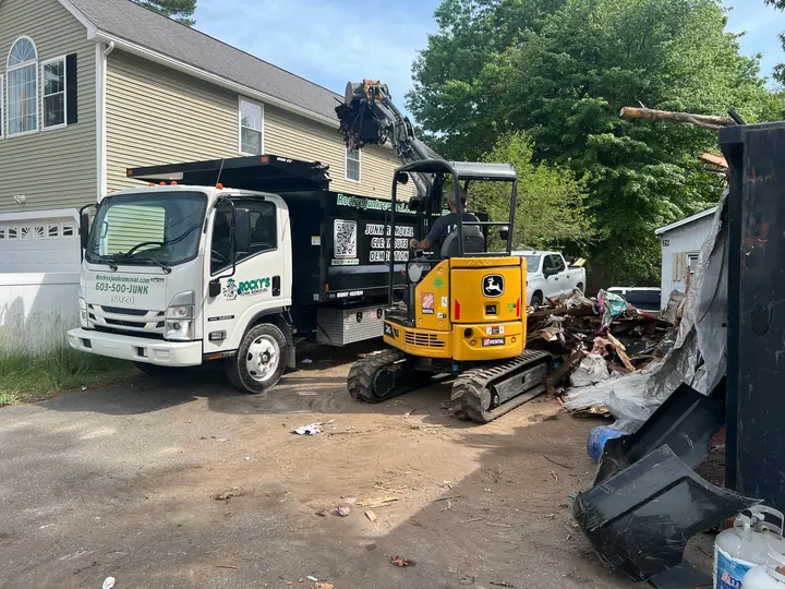 Rocky's Junk Removal truck and a mini excavator loading a large pile of debris