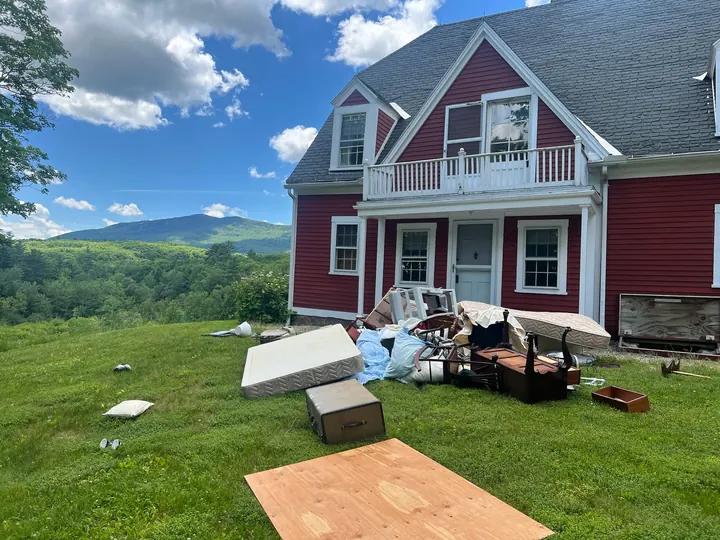 Furniture, mattresses and boxes piled on the lawn in front of a red house before pickup