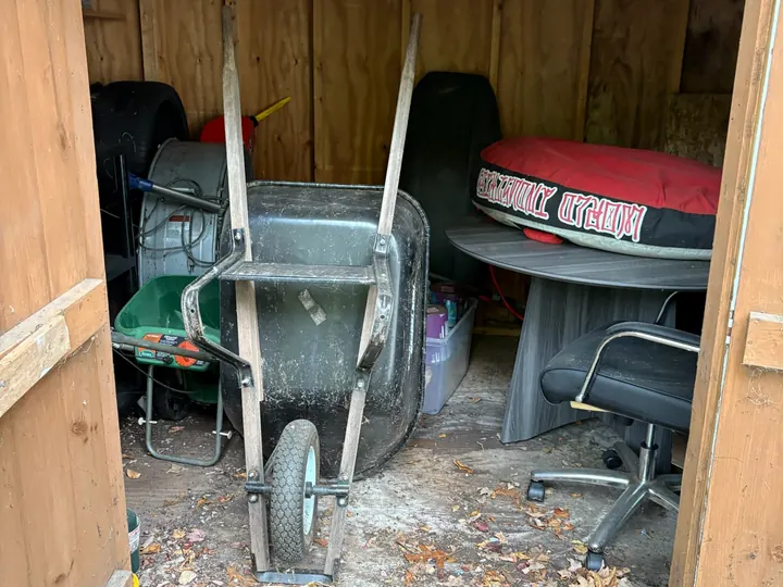 Storage shed full of tools, a wheelbarrow and furniture before Rocky's Junk Removal cleared it