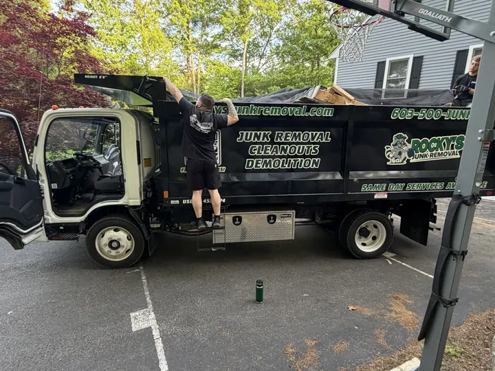 Rocky's Junk Removal truck with its door open and the bed loaded with junk at a Bedford, NH home