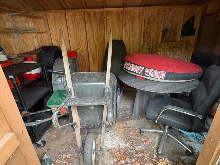 Inside of a Hudson, NH backyard shed packed with a wheelbarrow, chairs, and clutter before Rocky's cleanout