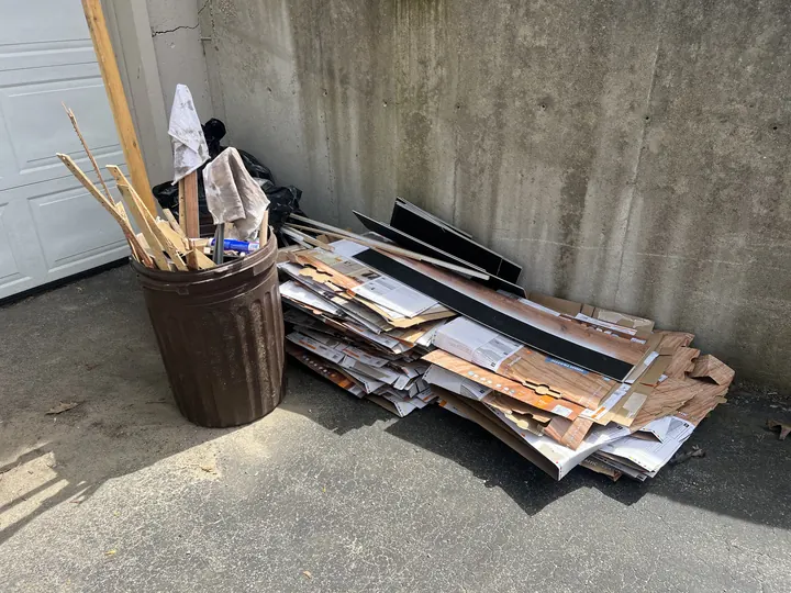 Pile of renovation debris, boards, and a trash barrel on a Nashua, NH garage floor before Rocky's hauled it away
