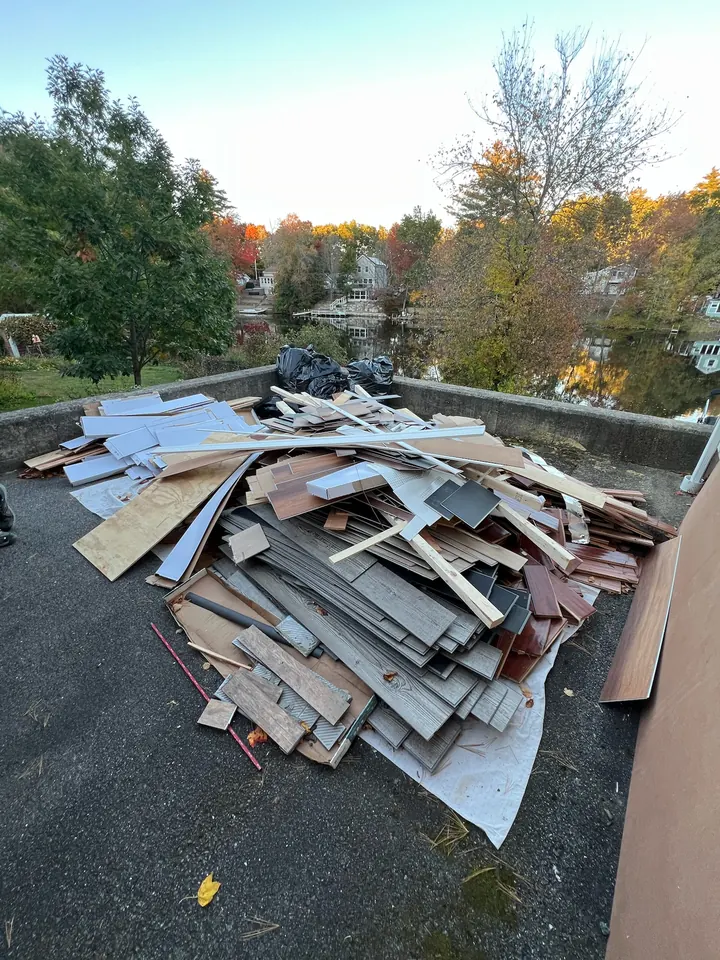 Pile of old flooring, trim, plywood, and bagged debris on a North Andover, MA driveway above the water before Rocky's hauled it