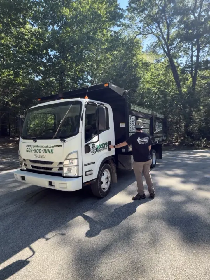 Rocky's Junk Removal dump truck in a tree-lined Pelham, NH driveway with a crew member beside it